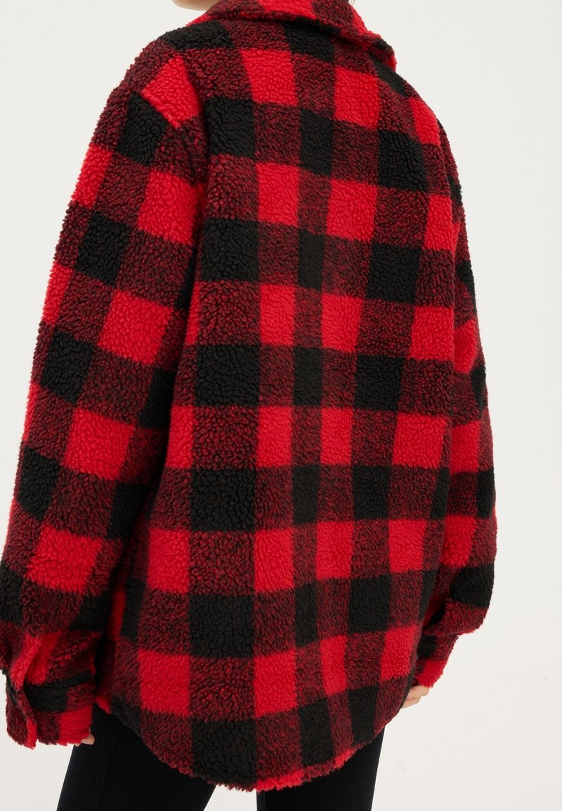 Rød og sort ternet fleece-skjortejakke med en tekstureret, fluffy overflade, lange ærmer og en løs pasform, med krave.