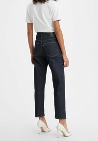 Mörka högmidjade jeans i denim med kontrasterande gula sömmar, raka ben och två bakfickor. Bärs med en vit T-shirt och klackar.