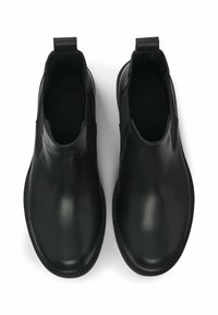 Pari mustavasta nahasta valmistettuja slip-on Chelsea-kenkiä, joissa on pyöreät varpaat ja kantapäässä vetolenkit, nähtynä ylhäältä valkoista taustaa vasten.