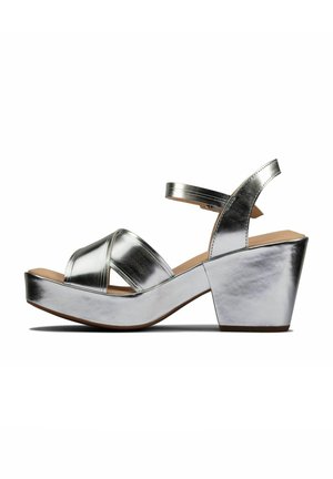 Sølvmetallic platform sandaler med åbne tæer og krydsede remme, med en kraftig hæl og glat tekstur.