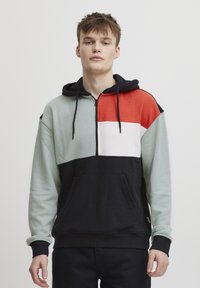 Felpa con cappuccio caratterizzata da una chiusura con zip, design a blocchi di colore in verde menta, rosso, bianco e nero; include tasca frontale e cordino.