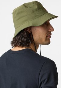 Cappello a secchiello verde oliva con visiera ampia, realizzato in tessuto morbido. Presenta un cordino regolabile e un piccolo logo sul davanti.
