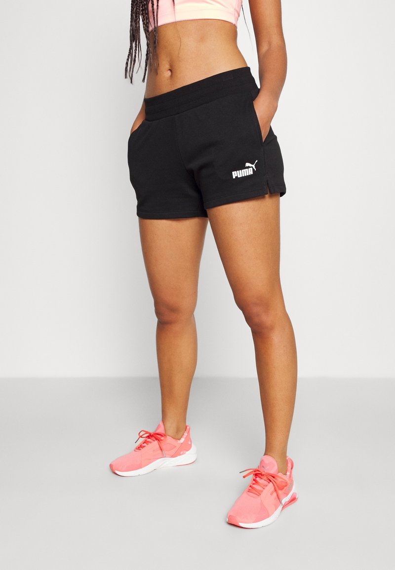 Black cotton shorts with side pockets, featuring a wide elastic waistband and white Puma logo. Paired with pink athletic shoes.