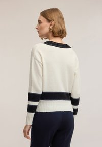 Sweter robiony na drutach w kolorze kremowym z granatowymi i metalicznymi paskami. Posiada okrągły dekolt, ściągacze na rękawach i luźny krój, podkreślający miękką fakturę.