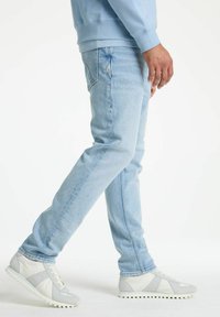 Svijetloplave traperice ravnog kroja, s izblijedjelim detaljima, u kombinaciji s višebojnim sivim tenisicama sa teksturiranim potplatima.