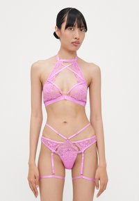 Pink lace lingerie set featuring a halter bra with crisscross straps and matching panties with garter straps. Detailed floral patterns throughout.