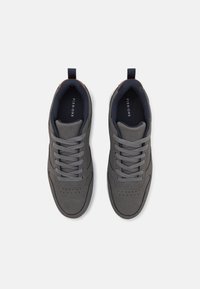 Gray sneaker with soft suede upper, round toe, stitched detailing, and rubber sole. Features gray laces and a brown accent at the heel.