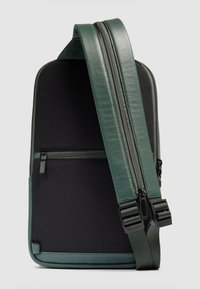 Groene en zwarte rugzak met een textuur van gaas aan de voorkant, leren accenten, twee vakken met rits en een verstelbare band.