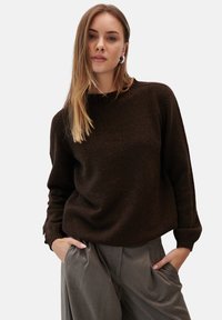 Brązowy sweter dzianinowy z okrągłym dekoltem i ribbowymi mankietami, połączony z jasnoszarymi spodniami o szerokich nogawkach. Gładka tekstura i luźny krój.