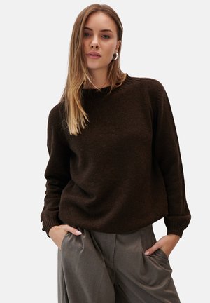 Brązowy sweter dzianinowy z okrągłym dekoltem i ribbowymi mankietami, połączony z jasnoszarymi spodniami o szerokich nogawkach. Gładka tekstura i luźny krój.