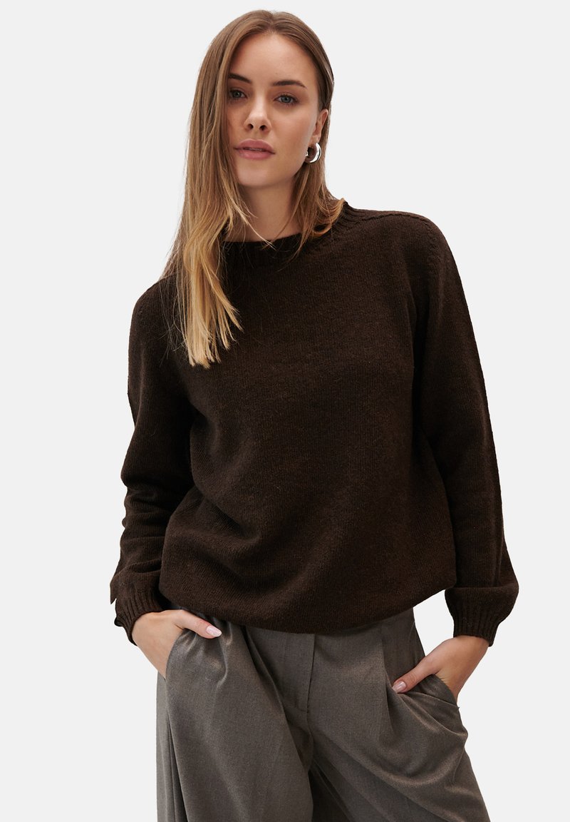 Brązowy sweter dzianinowy z okrągłym dekoltem i ribbowymi mankietami, połączony z jasnoszarymi spodniami o szerokich nogawkach. Gładka tekstura i luźny krój.