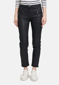 Černé slim-fit kalhoty vyrobené z elastického materiálu, s kapsami na zip a hladkým povrchem. Nosí se s bílými teniskami.