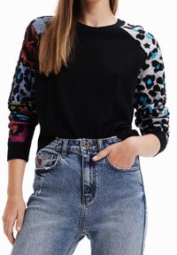 Black sweater with multicolored patterned sleeves, round neckline, and ribbed cuffs, paired with high-waisted faded blue jeans.