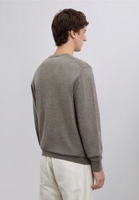 Ljusgrå stickad tröja med långa ärmar och rund halsringning. Har ribbade muddar och fåll, slät textur och en enkel design utan utsmyckningar.