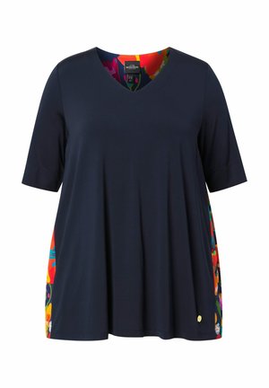 Top azul marino con escote en V y mangas cortas, con paneles laterales florales coloridos y un pequeño emblema dorado cerca del dobladillo.