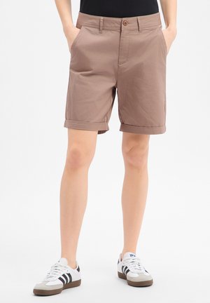 Osoba nosząca brązowe szorty do kolan z podwiniętymi brzegami i kieszeniami, w połączeniu z białymi i czarnymi trampkami oraz czarnym topem.