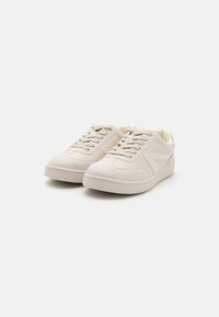 Jasnobeżowe sneakersy z gładkiej skórzanej cholewki, zaokrąglonym noskiem, płaskimi sznurowadłami i teksturowaną gumową podeszwą; minimalistyczny design z bocznymi akcentami.