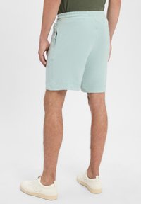 Mintgrüne Sportshorts aus weichem Stoff mit einem elastischen Bund, seitlichen Taschen und krempelbaren Säumen, kombiniert mit weißen Sneakers.