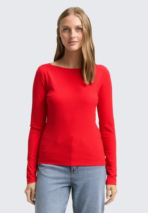 Haut à manches longues rouge en maille côtelée avec un col bateau, texture lisse et coupe ajustée, associé à un jean bleu clair.