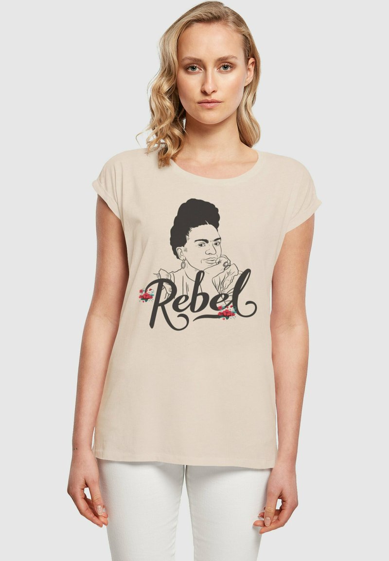Beige T-Shirt mit kurzen, aufgerollten Ärmeln, versehen mit einer schwarzen Linzeichnung eines Frauenkopfes und dem Wort "Rebel" in einer eleganten Schriftart, akzentuiert mit Blumen.