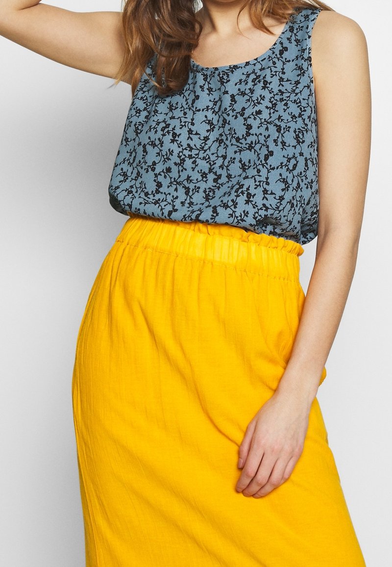 Haut sans manches à motifs floraux bleus associé à une jupe jaune vif, taille haute, texturée, avec une ceinture élastique.