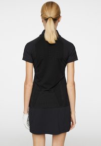 Czarna sukienka z krótkim rękawem, z teksturowanym siateczkowym tyłem, z kołnierzykiem polo i długością sięgającą powyżej kolan. Biała rękawiczka na lewej ręce.