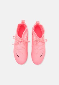 Pari urheilullisia kirkkaan vaaleanpunaisia kenkiä, joiden nauhat on sidottu rusetiksi, mustat Nike-logot varpaissa ja vetotapit kantapäässä, valkoista taustaa vasten.