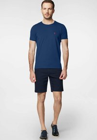 Granatowy bawełniany t-shirt z krótkimi rękawami i okrągłym dekoltem, z małym czerwonym logo. Do tego ciemne szorty i sportowe buty.