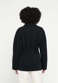 Palton negru cu cordon, cu design croit, având un guler larg și croială lejeră. Partea din spate include pliuri pentru un plus de textură.