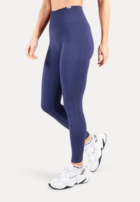 Leggings bleu marine taille haute en tissu extensible avec une texture lisse et des coutures sculptantes. Associés à des baskets blanches de sport.