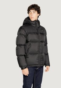 Giubbotto a bolla nero con cappuccio, caratterizzato da un design trapuntato e tasche con zip. Il materiale appare lucido ed è isolato per il calore.