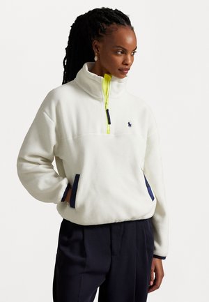 Pull en polaire blanc avec demi-fermeture éclair, accents jaune vif et poches en bleu marine. Présente un petit logo brodé.