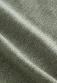 Miękka, jasno szarozielona tkanina o delikatnej fakturze dzianiny, z łagodnymi fałdami tworzącymi subtelne cienie i refleksy świetlne.