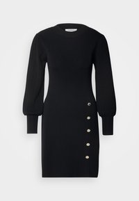 Robe noire en maille côtelée à manches longues avec des manches ballons et cinq boutons métalliques alignés verticalement sur le côté droit de la jupe.
