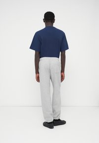 Granatowy bawełniany t-shirt z krótkim rękawem, zestawiony z jasnoszarymi dresowymi spodniami z elastycznym pasem, bocznymi kieszeniami i ściągaczami przy kostkach. Czarne buty.