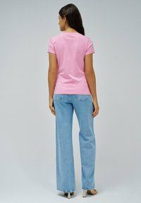 Camiseta de algodón rosa de manga corta, combinada con unos vaqueros de pierna ancha de cintura alta de color azul claro. Modelo visto desde la espalda, con el pelo liso.