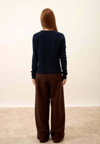 Granatowy sweter ściągaczowy z długimi rękawami, w parze z szerokimi brązowymi spodniami. Tekstura wydaje się miękka, a krój jest luźny.