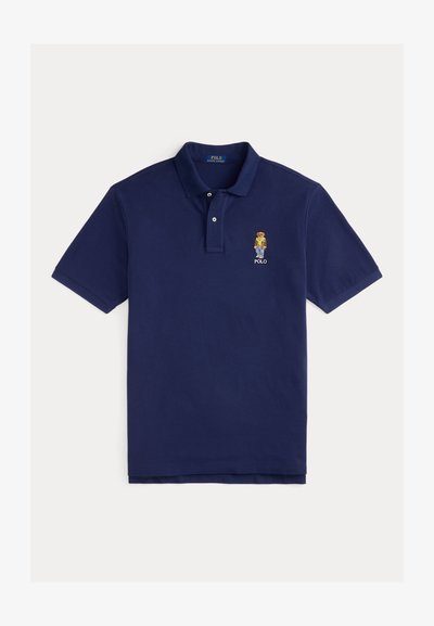 Tums zila kokvilnas polo krekls ar apkakli, diviem pogām, īsām piedurknēm un nelielu izšūtu varoņa logotipu uz krūtīm.