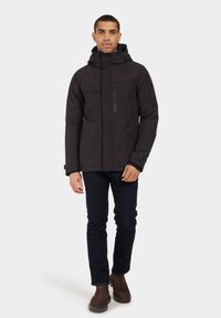 Črna nepremočljiva jakna s kapuco, vidnim zadrgo in več žepi. Prilega se telesu, ima gladko teksturo in brez vidnih vzorcev.