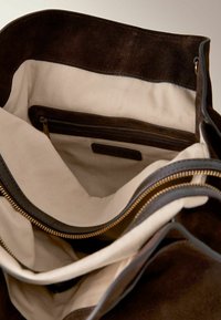 Bruine suede handtas met een beige canvasvoering, ritsvak en gouden ritshardware. Gladde randen en stevige constructie.
