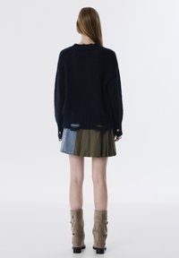 Pull en maille bleu marine à coupe décontractée, avec un ourlet côtelé, associé à une jupe plissée olive et des bottines beiges.