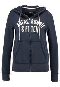 Navyblauwe zip-up hoodie van zachte stof, met een wit logo op de borst, twee voorkennis en een capuchon met trekkoord.