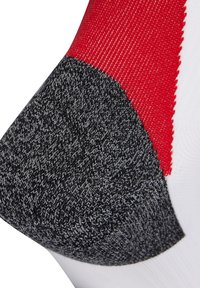 Calcetín con una combinación de colores rojo, negro y blanco, con un talón texturizado en gris y una tela blanca suave. Detalle de costura reforzada evidente.