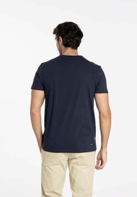 T-shirt en coton bleu marine avec un col rond et des manches courtes. Texture lisse, détail de logo près de l'ourlet et coupe décontractée.