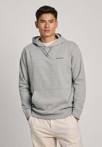 Sivi dukserica s kapuljačom i vezicom, prednjim džepom i "Pepe Jeans" logom. Ima opušteni kroj i rebraste manžete. Nosii se preko bijele majice.