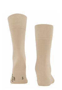 Calcetas beige con parte superior acanalada y textura suave. Marcadas con texto negro cerca del tobillo. Diseño alargado y ajustado.