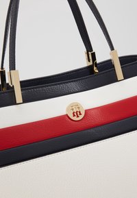 Rakennettu käsilaukku, jossa on nahkaa sinivalko-punaisilla raidoilla. Kultaiset metalliosat ja logotieto edessä.