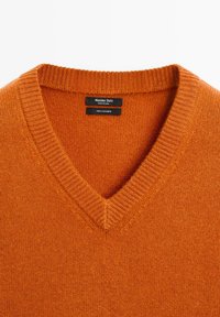V-Ausschnitt Kaschmirpullover in leuchtendem Orange. Weicher Stoff mit geripptem Ausschnitt. Etiketten geben Marke, Herkunft und Materialzusammensetzung an.