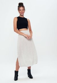Top corto nero a costine con scollo rotondo abbinato a una gonna midi chiara a fantasia con spacco laterale, indossata con stivali alla caviglia neri.