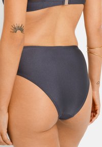 Augsta vidukļa bikini apakša tumši zilā audumā, ar gludu tekstūru, bezšuvju dizains un minimāli redzamas diegu šuves.